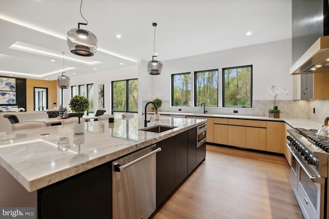 kitchen with wall chimney range hood, a sink, modern cabinets, appliances with stainless steel finishes, and recessed lighting