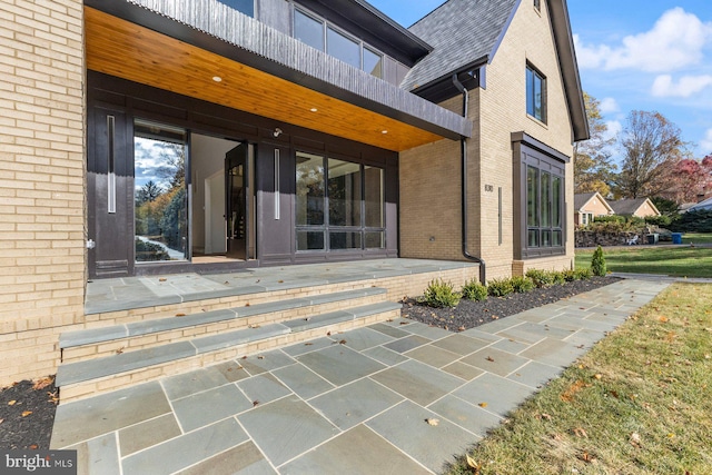 rear view of property featuring brick siding, roof with shingles, and a balcony
