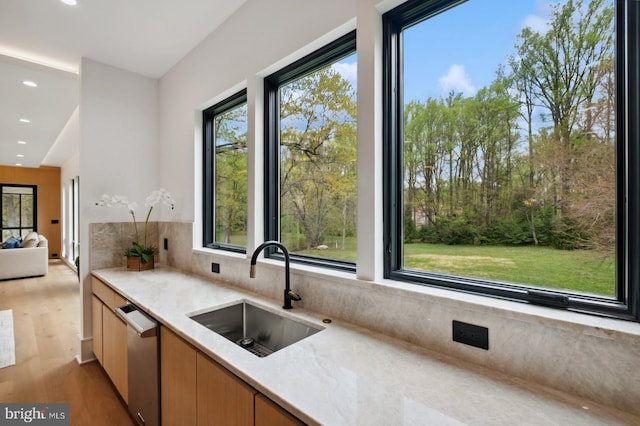 kitchen with recessed lighting, stainless steel dishwasher, a sink, light wood-style floors, and light stone countertops