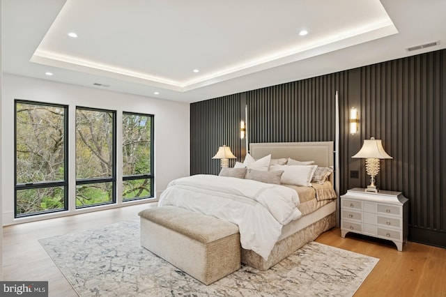 bedroom with light wood finished floors, visible vents, recessed lighting, and a raised ceiling