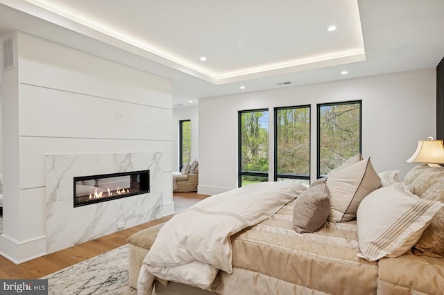 bedroom featuring a premium fireplace, wood finished floors, a raised ceiling, visible vents, and recessed lighting