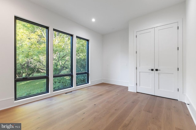 unfurnished bedroom featuring recessed lighting, light wood-type flooring, a closet, and multiple windows