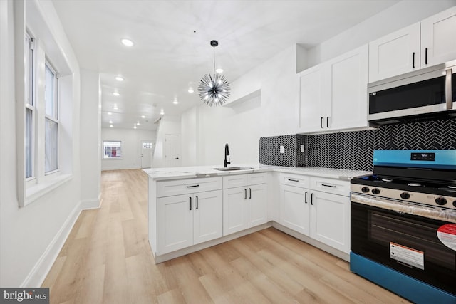 kitchen featuring white cabinets, stainless steel appliances, a sink, light wood-type flooring, and a peninsula