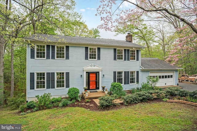 colonial-style house with a chimney, an attached garage, driveway, and a front yard
