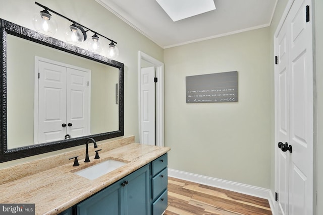 bathroom featuring baseboards, a skylight, wood finished floors, vanity, and ornamental molding