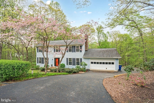 colonial house with a chimney, aphalt driveway, and a garage