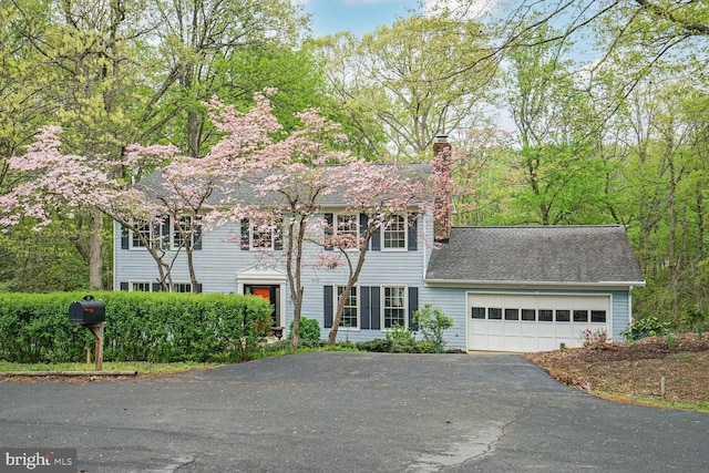 colonial home featuring driveway, a chimney, roof with shingles, and a garage