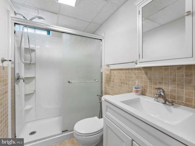 bathroom featuring tile walls, a shower stall, a drop ceiling, and toilet