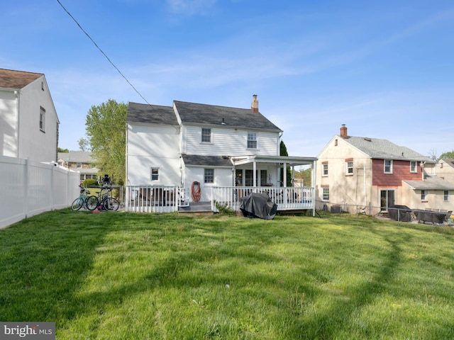 back of house featuring a lawn, a fenced backyard, a chimney, and a deck