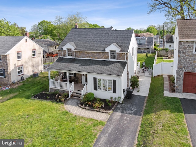 view of front facade with a porch, driveway, a front yard, fence, and a shingled roof