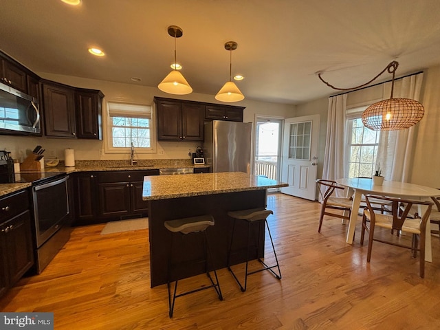 kitchen featuring stainless steel appliances, a center island, a sink, dark brown cabinetry, and light stone countertops