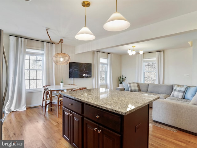 kitchen with light wood finished floors, decorative light fixtures, light stone countertops, a kitchen island, and open floor plan
