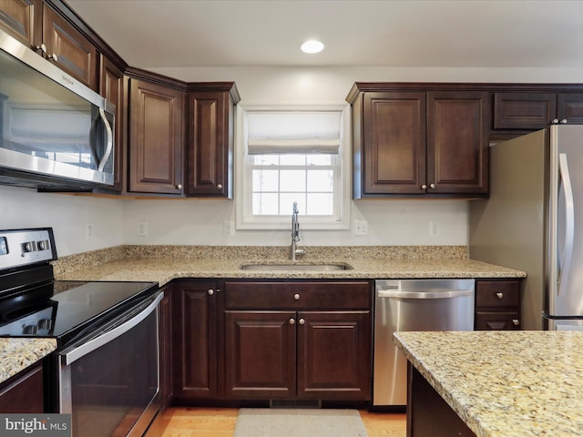 kitchen featuring recessed lighting, light stone counters, stainless steel appliances, a sink, and dark brown cabinetry