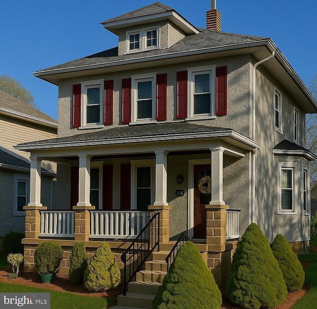 american foursquare style home featuring a porch, a chimney, and stucco siding