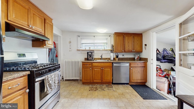 kitchen featuring radiator, stainless steel appliances, under cabinet range hood, brown cabinetry, and a sink
