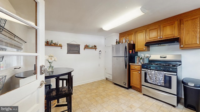 kitchen with appliances with stainless steel finishes, under cabinet range hood, brown cabinets, light flooring, and baseboards