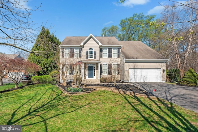 colonial house featuring a front lawn, aphalt driveway, and a garage