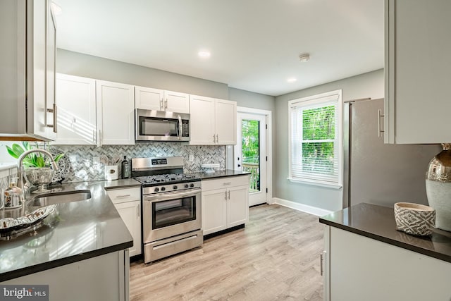 kitchen featuring stainless steel appliances, a sink, white cabinetry, tasteful backsplash, and light wood-type flooring