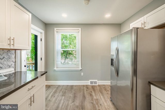 kitchen with stainless steel fridge, dark countertops, light wood-style floors, white cabinetry, and baseboards