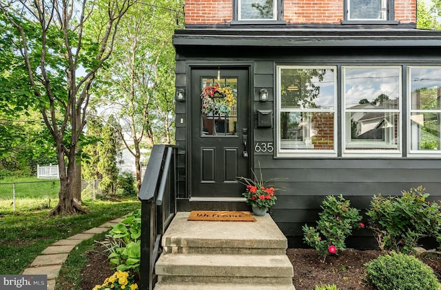 view of exterior entry with fence and brick siding
