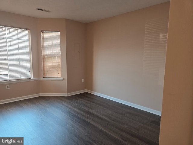 spare room featuring baseboards, visible vents, dark wood-style floors, and a healthy amount of sunlight