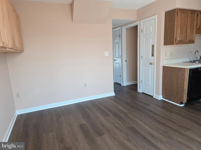 kitchen featuring dark wood finished floors, light countertops, dishwasher, a sink, and baseboards