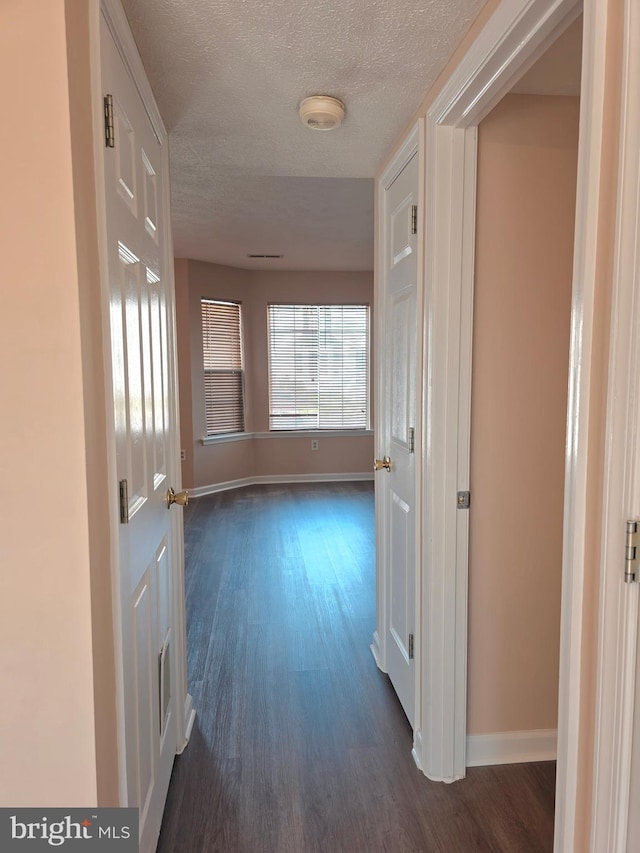hallway with a textured ceiling, baseboards, and dark wood-style flooring