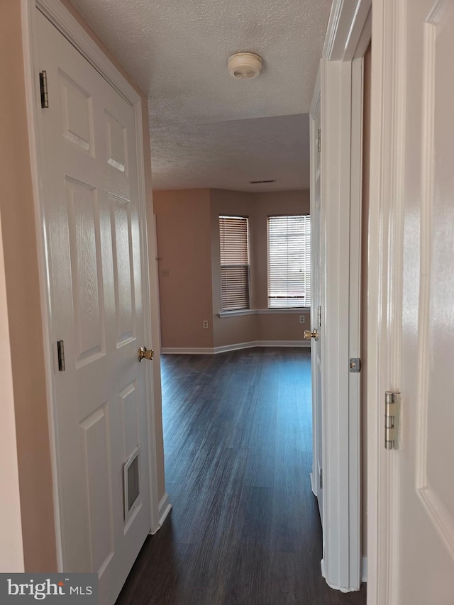 hallway with baseboards, dark wood-style flooring, a textured ceiling, and visible vents
