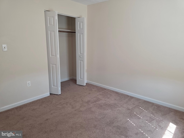 unfurnished bedroom featuring baseboards, carpet flooring, and a closet