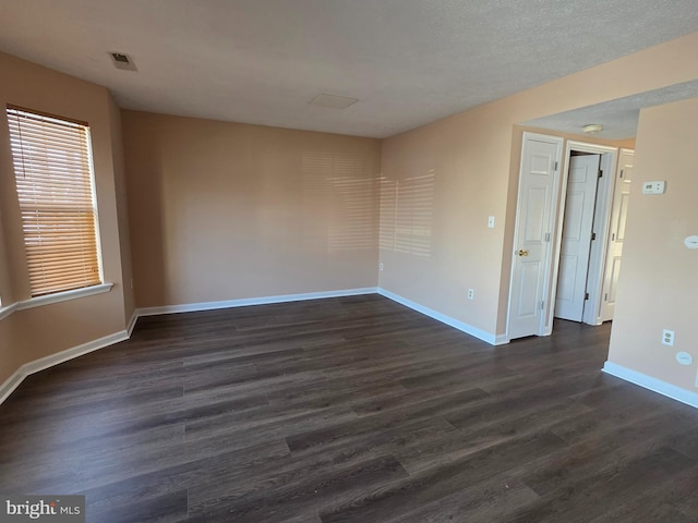 unfurnished room with baseboards, visible vents, and dark wood finished floors