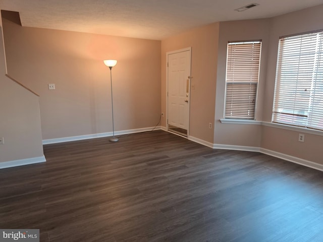 spare room with visible vents, baseboards, and dark wood-style floors