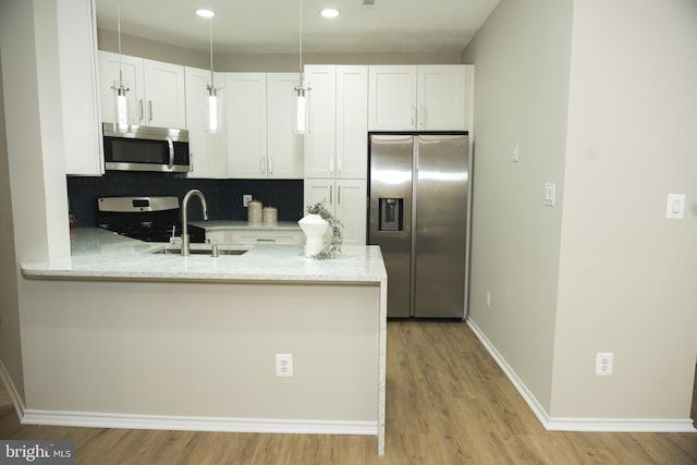 kitchen with a peninsula, white cabinetry, stainless steel appliances, and a sink