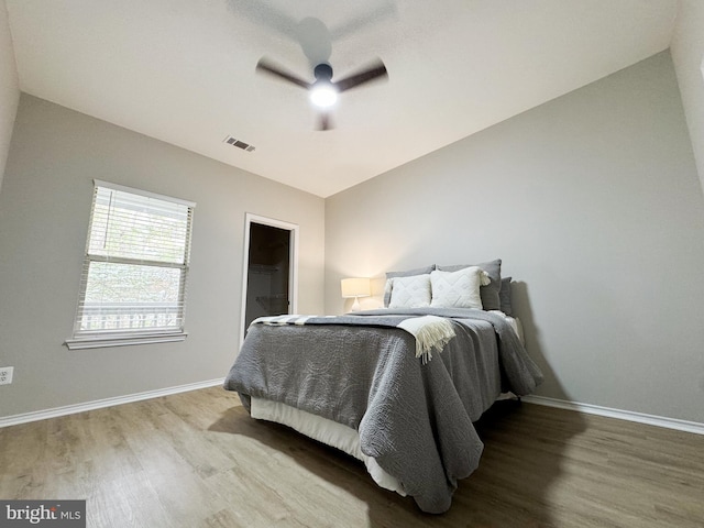 bedroom featuring baseboards, a spacious closet, visible vents, lofted ceiling, and wood finished floors