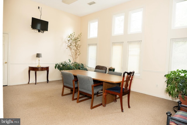 dining space featuring carpet, visible vents, and a towering ceiling