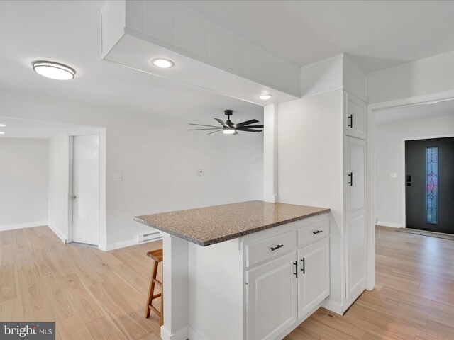 kitchen with baseboard heating, dark stone counters, ceiling fan, light wood finished floors, and white cabinets