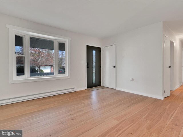 empty room featuring light wood-type flooring, baseboards, and a baseboard heating unit