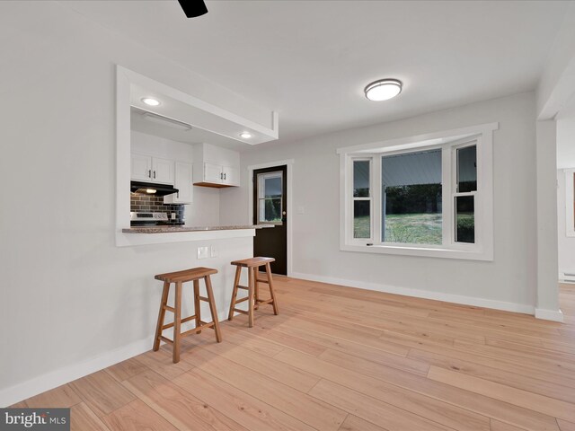 kitchen with white cabinets, baseboards, a kitchen breakfast bar, and under cabinet range hood