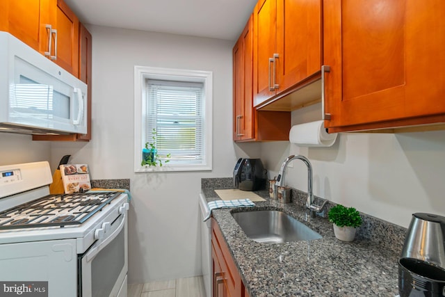 kitchen featuring brown cabinets, dark stone countertops, a sink, and white appliances
