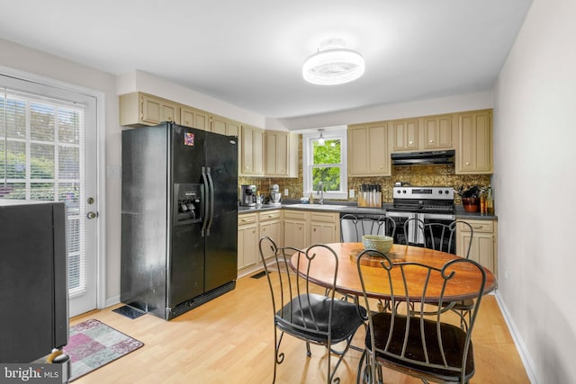 kitchen with cream cabinets, black fridge, stainless steel range with electric stovetop, backsplash, and under cabinet range hood