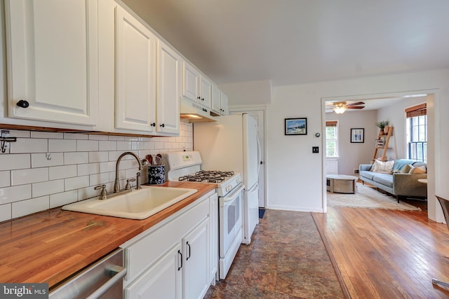 kitchen with white gas stove, a sink, wood counters, white cabinets, and tasteful backsplash