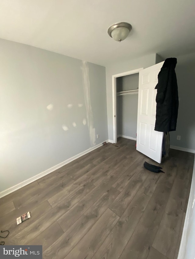 unfurnished bedroom featuring baseboards, a closet, and dark wood-style flooring