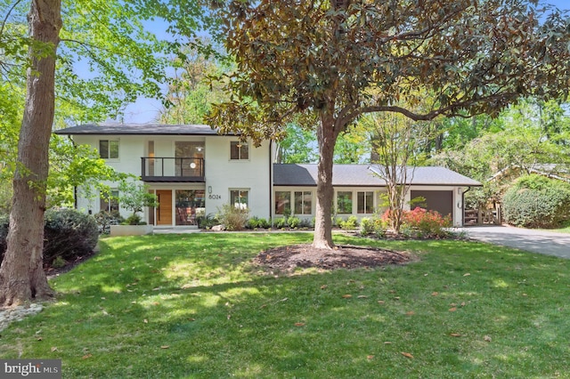 traditional-style home featuring concrete driveway, a balcony, a front yard, and a garage