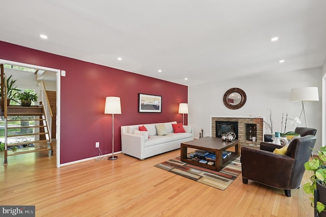 living room with stairs, a glass covered fireplace, wood finished floors, baseboards, and recessed lighting