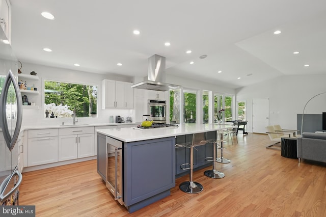 kitchen featuring island exhaust hood, appliances with stainless steel finishes, a sink, wine cooler, and white cabinetry