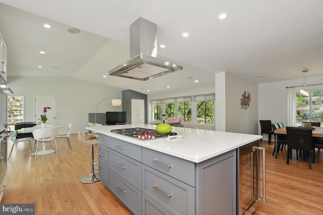 kitchen featuring a kitchen bar, island exhaust hood, gray cabinetry, beverage cooler, and stainless steel gas stovetop