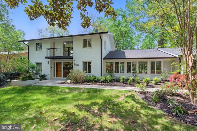 view of front of home with a front yard, brick siding, and a balcony