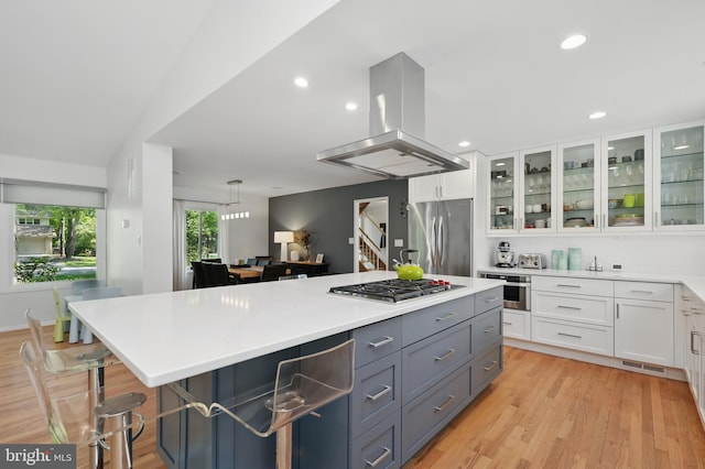kitchen with visible vents, island range hood, light countertops, white cabinetry, and appliances with stainless steel finishes