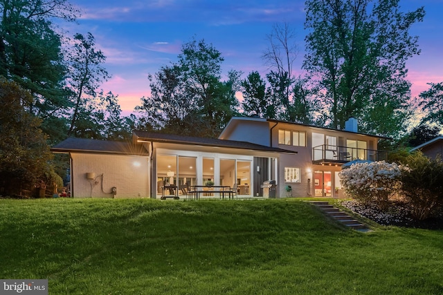 back of house at dusk featuring a lawn, a sunroom, and a balcony