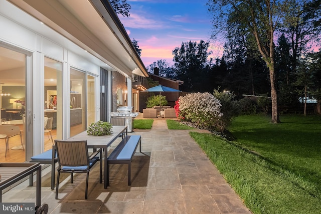 patio terrace at dusk with an outdoor living space, outdoor dining area, a lawn, and grilling area
