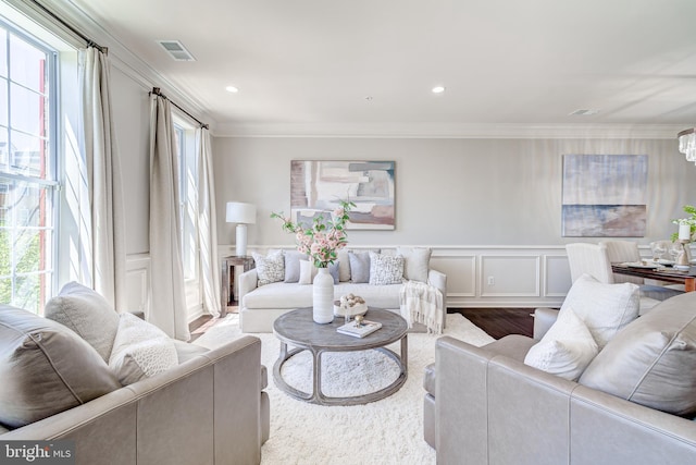 living area with wainscoting, a decorative wall, wood finished floors, visible vents, and ornamental molding